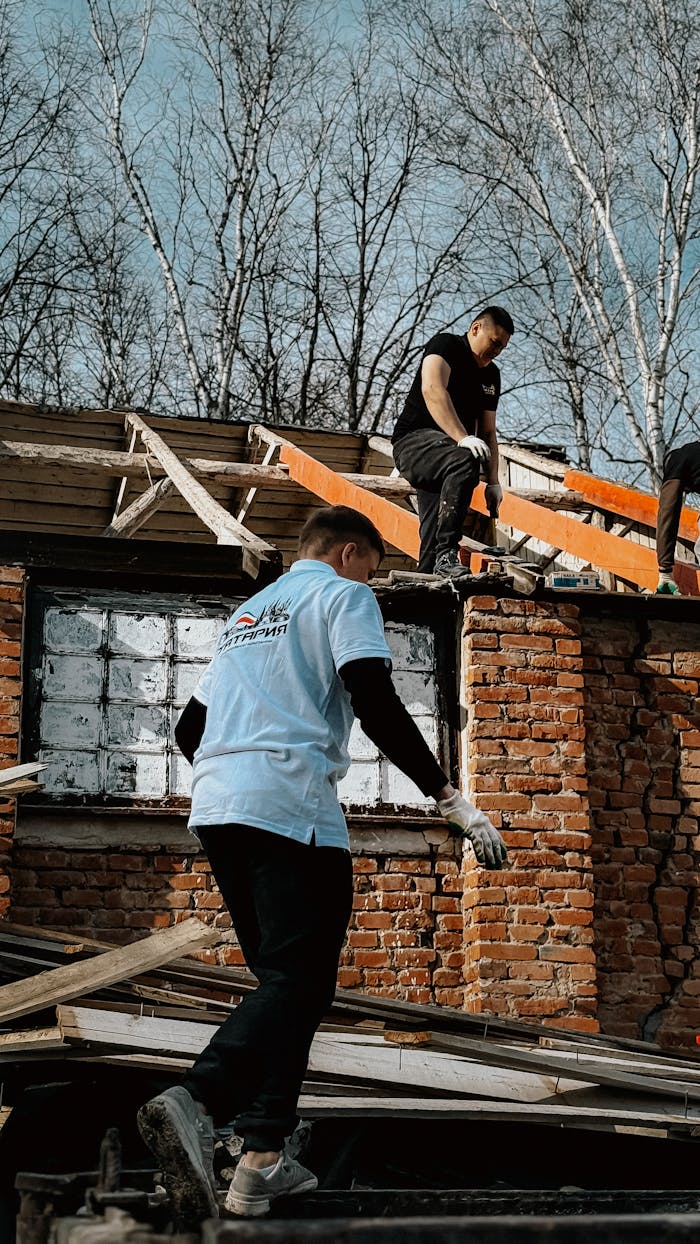Two men working on roof construction of a brick building during daytime.